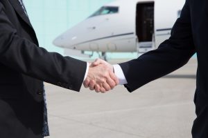 Business people shaking hands in front of a corporate jet